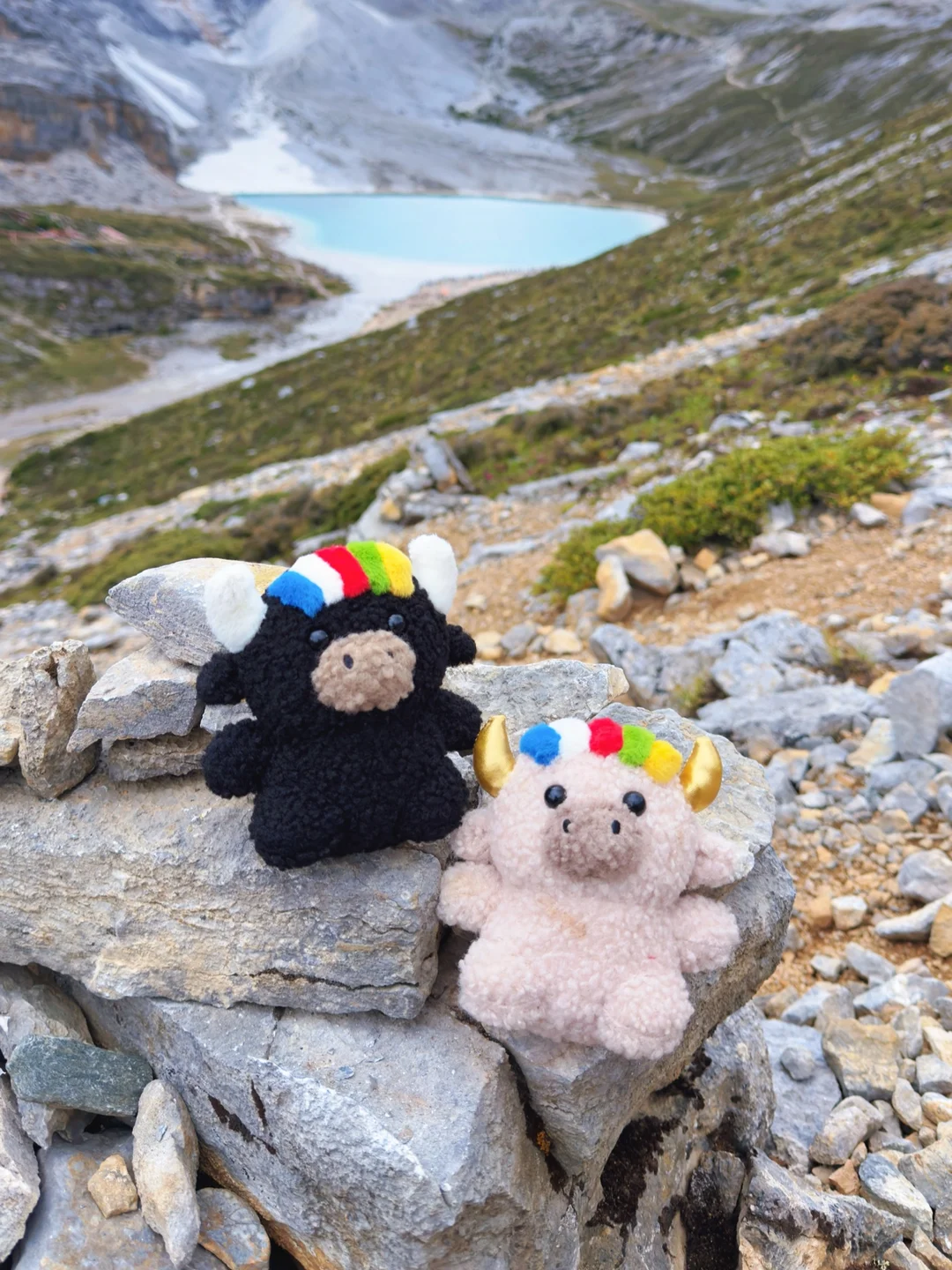 Tashi and Dele on rocks above a turquoise snow-mountain lake — 雪山湖邊的扎西與德勒
