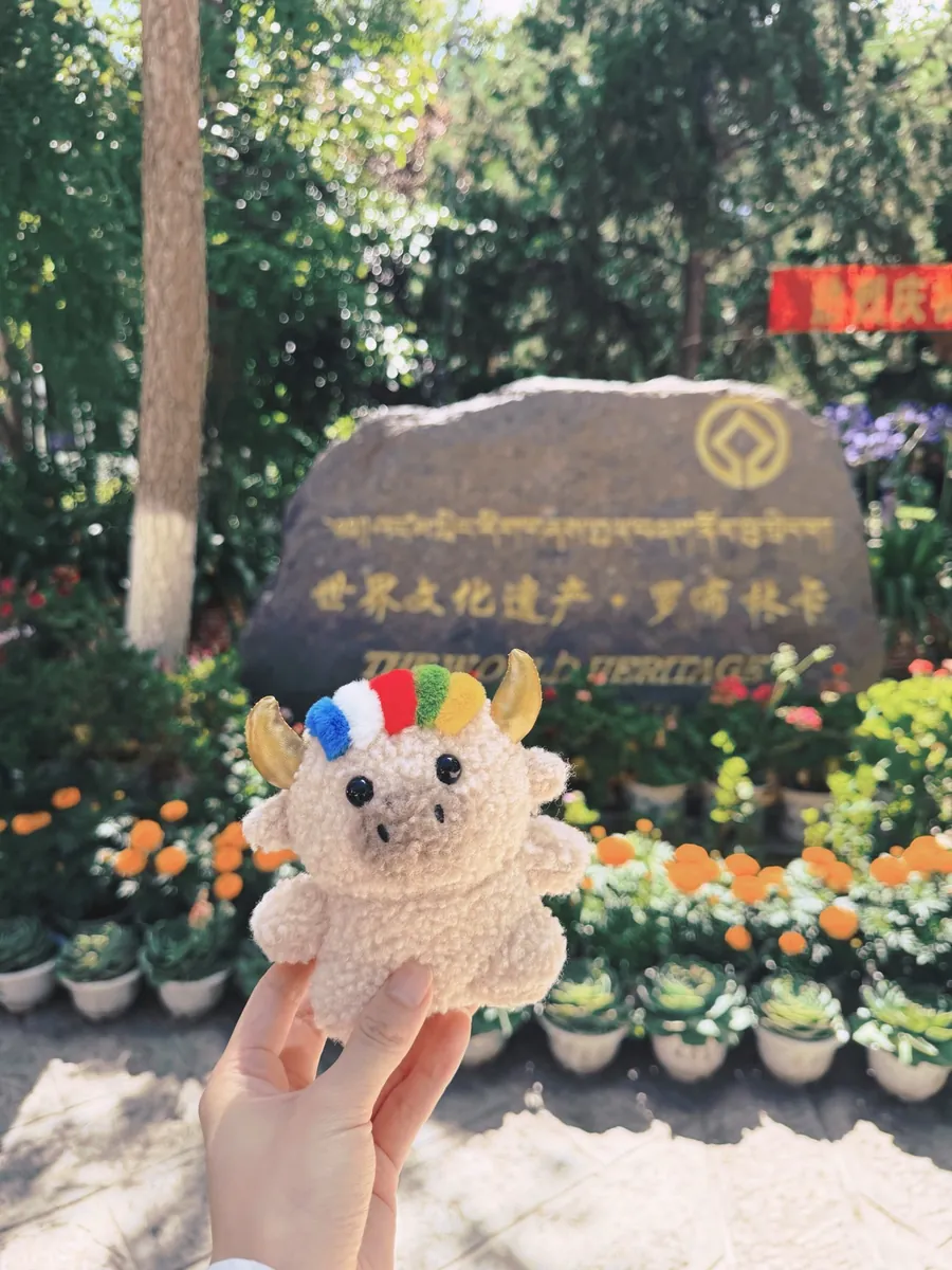 Dele held up in front of the World Heritage stone at Norbulingka, flowers all around — 羅布林卡世界文化遺產石碑前的德勒